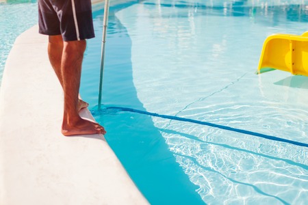Man cleaning hotel swimming pool with vacuum tube cleaner in the morning. Worker taking care of poolの写真素材