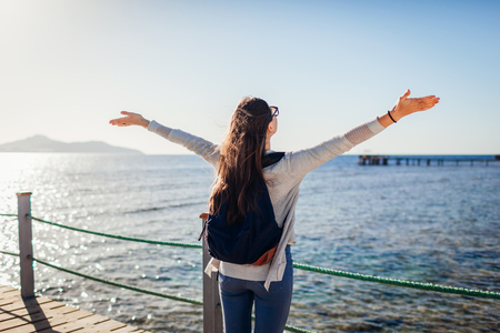 Young female tourist with backpack admiring landscape of Red sea and Tiran island on pier. Traveling concept. Summer vacationの写真素材