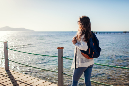 Young female tourist with backpack admiring landscape of Red sea and Tiran island walking on pier. Traveling concept. Summer vacationの写真素材