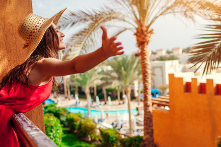 Young woman enjoying the view from hotel balcony in Egypt. Happy tourist feeling free with opened arms in tropical resortの写真素材