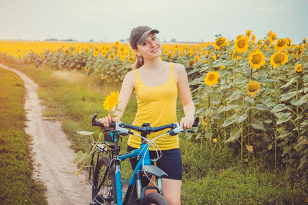 Young woman bicyclist riding in sunflower field before stormの写真素材