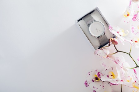 Female hand watch in gift box surrounded with orchid. Present for Women's day with flowers