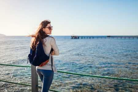Young female tourist with backpack admiring landscape of Red sea walking on pier. Traveling concept. Summer vacationの写真素材