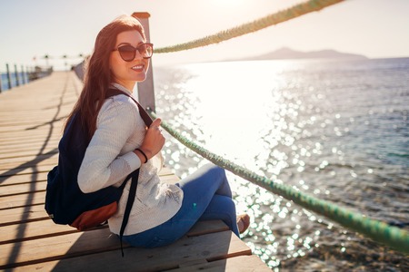 Young female tourist with backpack admiring landscape of Red sea and Tiran island sitting on pier. Traveling concept. Summer vacationの写真素材