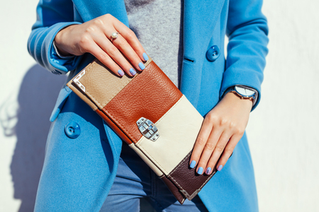 Young woman holding stylish handbag or clutch and wearing trendy blue coat. Spring female clothes and accessories. Fashionの写真素材