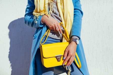 Young woman holding stylish yellow handbag and wearing trendy blue coat. Spring female clothes and accessories. Fashionの写真素材