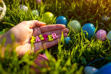 Happy Easter. Easter eggs in spring grass. Writing made of wooden letters in hand
