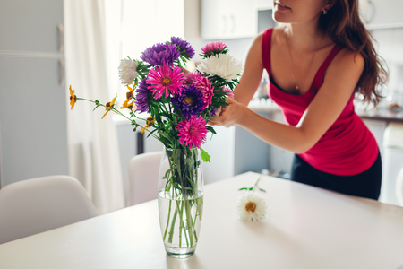 Woman puts flowers in vase. Housewife taking care of coziness in kitchen. Modern kitchen designの写真素材