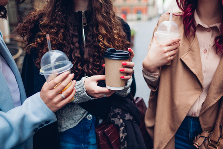 Three female friends having drinks outdoors. Happy women clinking coffee, orange juice and tea cupsの写真素材