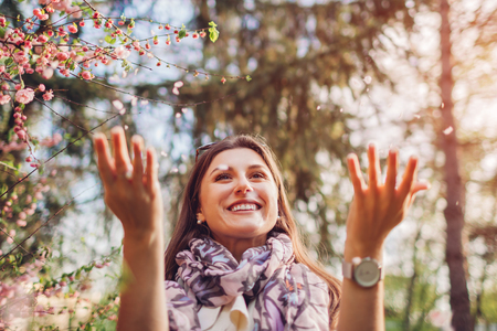 Beautiful happy woman throwing flower petals enjoying blooming spring garden. Having fun and...