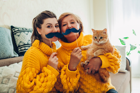 Senior mother and her adult daughter taking selfie with cat using photo booth props at home. Mother's day concept. Having funの写真素材