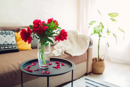 Interior of living room decorated with peonies flowers, plants and carpet. Cozy couch with cushions and tableの写真素材