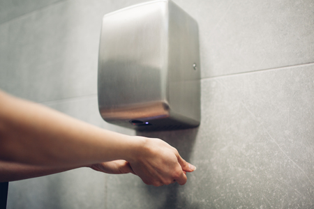 Air dryer in public toilet. Woman drying hands in water closet. Hygiene conceptの写真素材