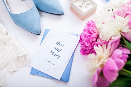 Wedding invitation surrounded with flowers, bride's blue shoes and jewellery. Morning of brideの写真素材