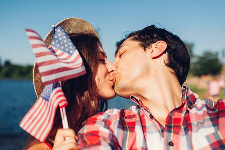 Couple in love kissing and holding USA flag against the blue sky. People celebrating Independence Day of Americaの写真素材