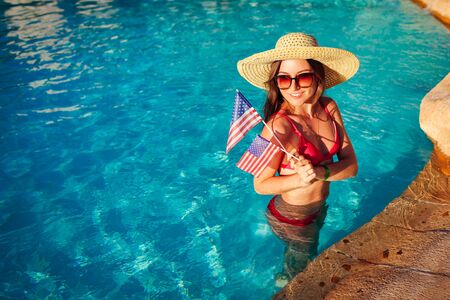 Sexy young woman holding USA flag in hotel swimming pool. Celebrating Independence day of Americaの写真素材