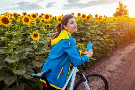 Young happy woman bicyclist riding bicycle in sunflower field. Summer sport activity. Healthy lifestyleの写真素材