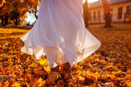 Woman dancing in autumn forestamoung orange and yellow maple leaves. Lady wearing stylish white skirt. Fall seasonの写真素材