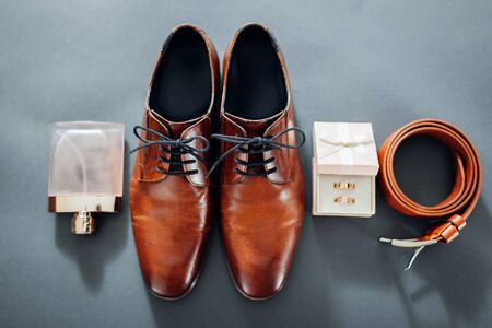 Groom's wedding day accessories. Brown leather shoes, belt, perfume, golden rings in box. Male fashionの写真素材