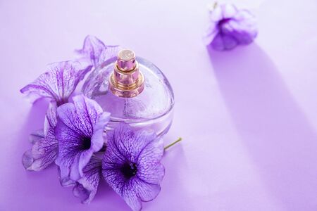 Bottle of perfume with flowers on purple background. Floral fragrance. Organic cosmeticsの写真素材