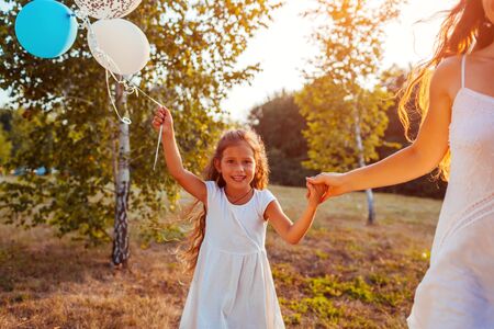 Little girl walking with mother and holding baloons in hand. Family having fun in summer parkの写真素材