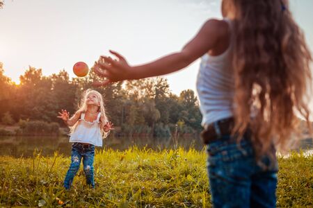 Little girls playing with ball in summer park. Kids having fun outdoors. Games for children. Sisters spending time togetherの写真素材