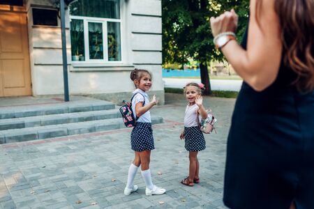 Happy mother waving to her daughters before classes outdoors primary school seeing them off. Family saying goodbye. First day of schoolの写真素材