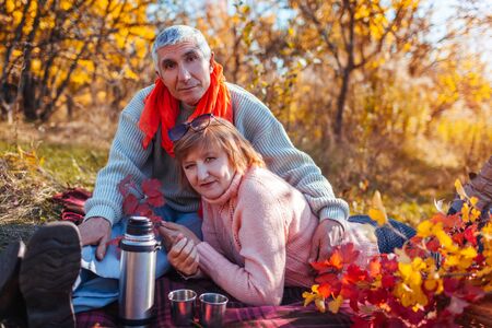 Senior couple having tea in autumn forest. Happy man and woman enjoying picnic and nature. Family timeの写真素材