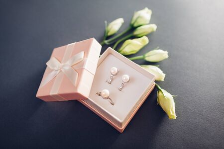 Set of pearl jewellery in gift box with flowers on grey background. Silver earrings and ring with...