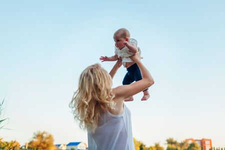 Young mother walking by summer river with baby girl. Woman lifting kid and having fun with child. Family spends time togetherの写真素材