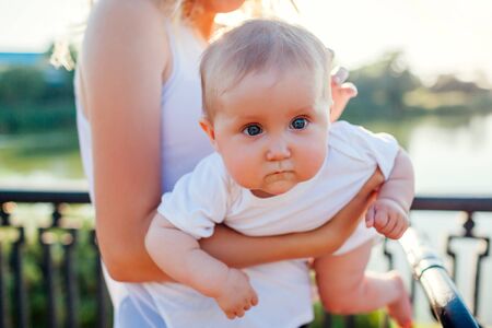 Young mother walking in summer park with her baby girl. Happy woman holding kid outdoors. Child looking at cameraの写真素材