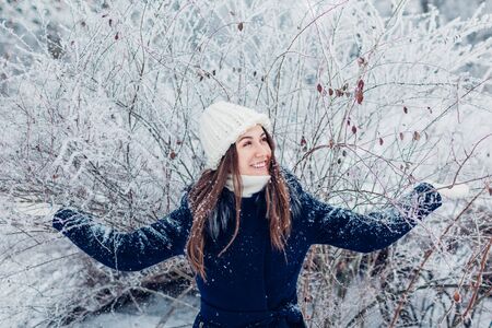 Winter activities. Young woman shaking branches with hoarfrost and snow in winter forest. Happy girl...