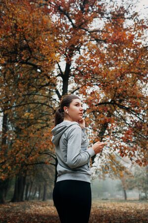 Woman is turning the music on for running in autumn forestの写真素材