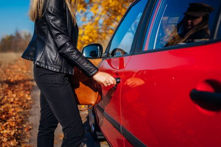 Opening car door. Woman opens red car with key on autumn road. Driver locks door upの写真素材