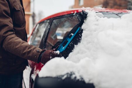Car cleaning from snow using broom. Man taking care of automobile window removing ice with brush outdoors. Winter weather conditionsの写真素材