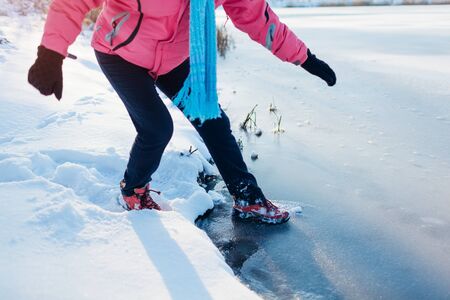 Dangerous thin ice. Woman takes risk to step on frozen river surface in winter. Caution, unsafe water, drop possibilityの写真素材