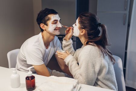 Woman applying clay mask on her husbands face. Young loving couple taking care of skin at home.の写真素材