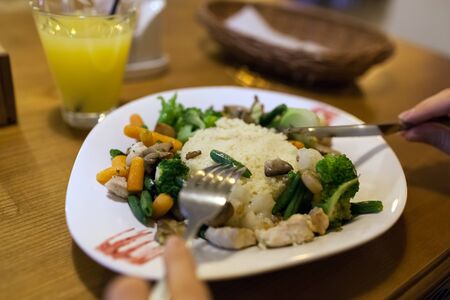 Couscous with chicken, fresh vegetables served with juice in restaurant. Woman eats dish with carrots, broccoli, mushrooms, cauliflower.の写真素材