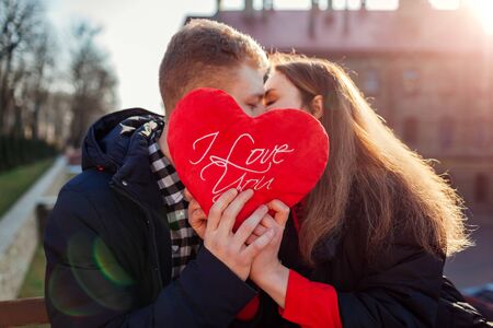 Valentines day kiss. Man and woman hiding behind heart shaped pillow with writing I love you...