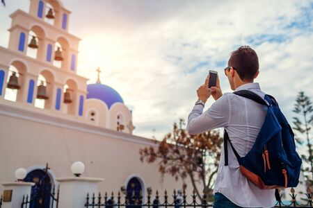 Santorini traveler man taking photo of St. Epifanios church in Akrotiri on smartphone. Tourism,...