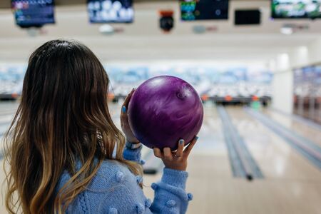 Bowling game. Woman having fun playing bowling in club. Girl holding ball ready to throw it and looking at screen with resultsの写真素材