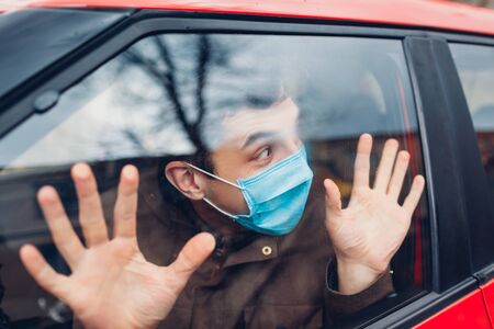 Driver man sitting in car wearing protective mask scared of sick coronavirus people outside. People panic. World pandemic dangerous fluの写真素材