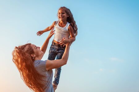 Mother's day. Woman playing having fun with daughter in spring park. Mother tossing girl outdoors and laughing. Family time. Spaceの写真素材
