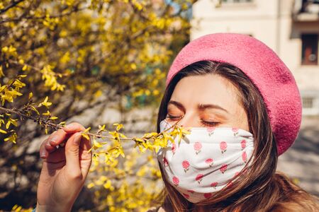 Woman wears reusable mask outdoors during coronavirus covid-19 pandemic. Girl smells spring flowers. Stay safe, positive. Spring fashionの写真素材