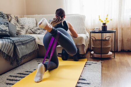 Home workout during coronavirus quarantine. Booty glutes building. Donkey kicks back. Woman training using mat sport belt.の写真素材