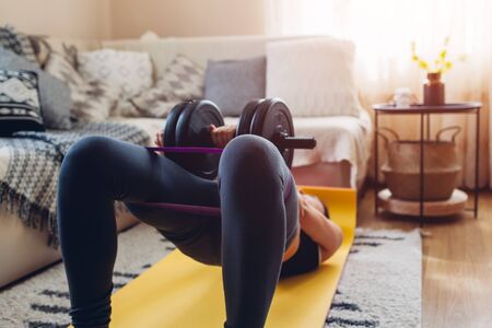 Home workout during coronavirus quarantine. Booty glutes building. Glutes bridge. Woman training using dumbbells mat sport belt.の写真素材