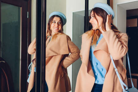 Woman looking at her reflection in mirror. Stylish girl trying spring clothes on with purse by wardrobe at home. Beauty fashionの写真素材