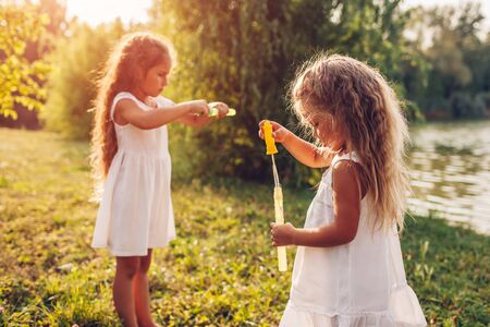 Little girls sisters blowing bubbles in spring park by river. Kids having fun playing games outdoors. Children activitiesの写真素材