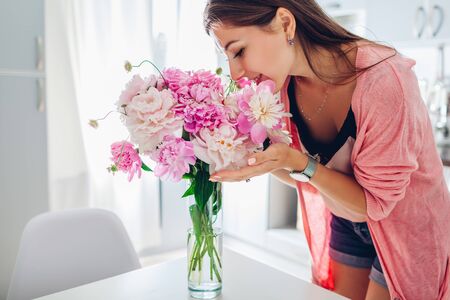 Happy woman smelling bouquet of peonies. Housewife enjoying decor and interior of kitchen. Sweet home. Allergy freeの写真素材