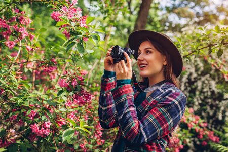 Woman photographer taking pictures using camera in summer garden shooting trees in blossom....